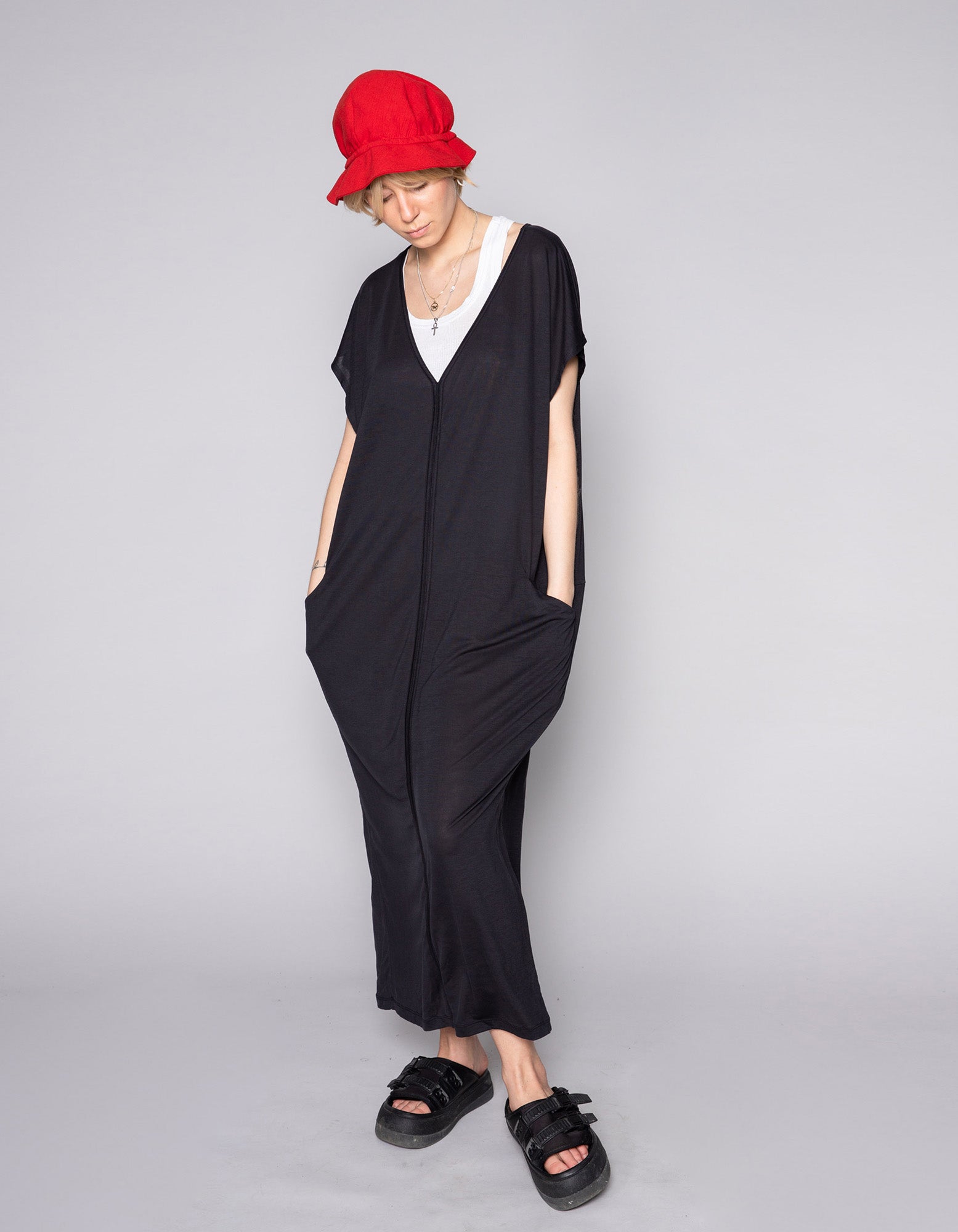 Model wearing the AWAN Kaftan Dress in warm black with a red hat, standing with hands in pockets.