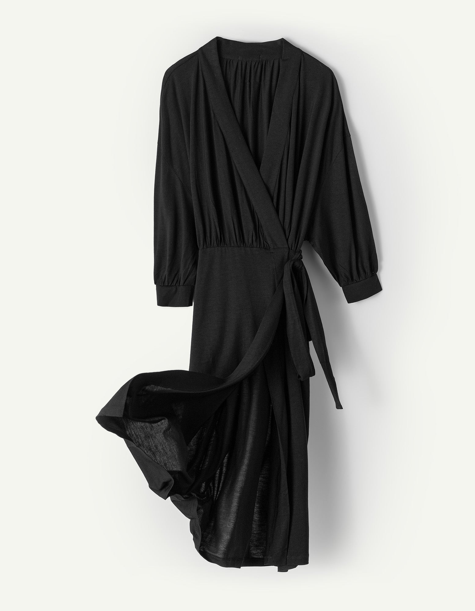 The AWAN Wrap Dress in warm black, made from silky soft Tencel™ lyocell jersey, features an adjustable waist belt and practical pockets. Perfect for work, parties, or lounging at home, this versatile dress offers comfort and style for any occasion.