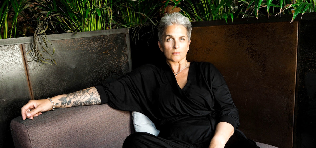 Confident silver-haired woman relaxing on a sofa wearing AWAN's black wrap cardigan and flow pants, made from 100% TENCEL Lyocell.